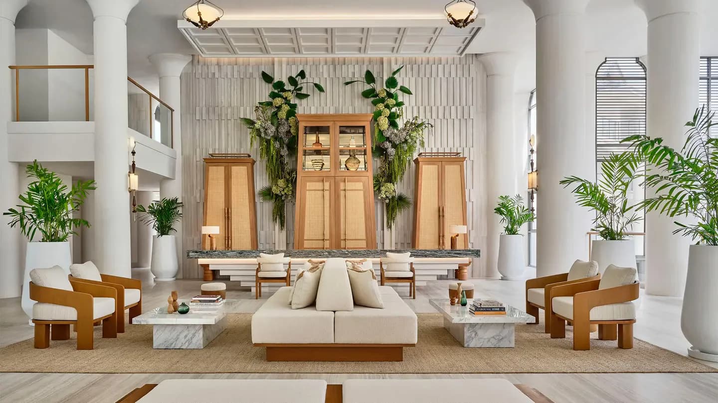 Symmetrical lobby interior with cream sofa, wooden doors, potted plants, and marble accents by Adam Farmerie.