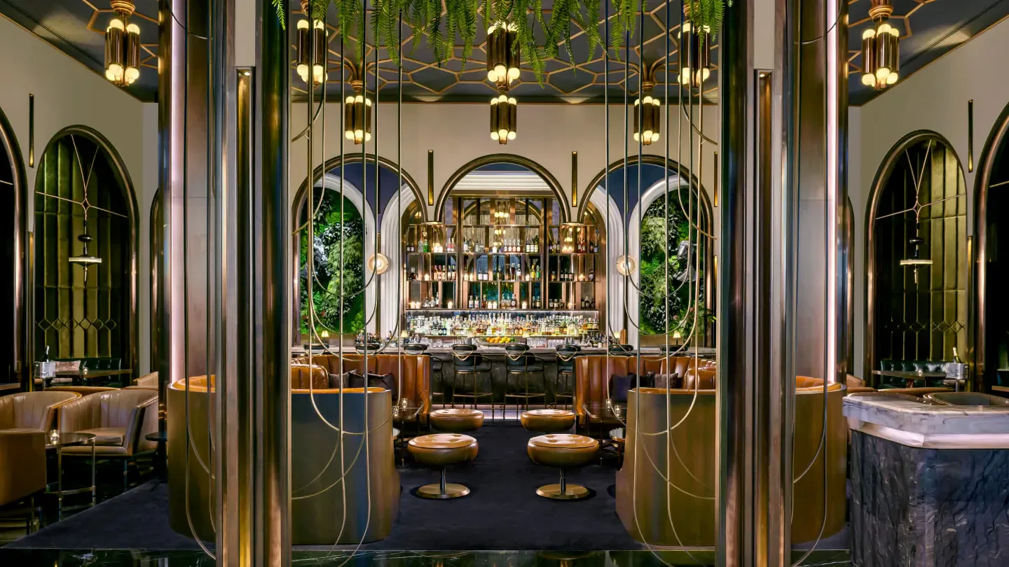 Luxurious bar lounge with symmetrical green arched doorways, brass hanging pendant lights, marble counters, and plush seating by Adam Farmerie.
