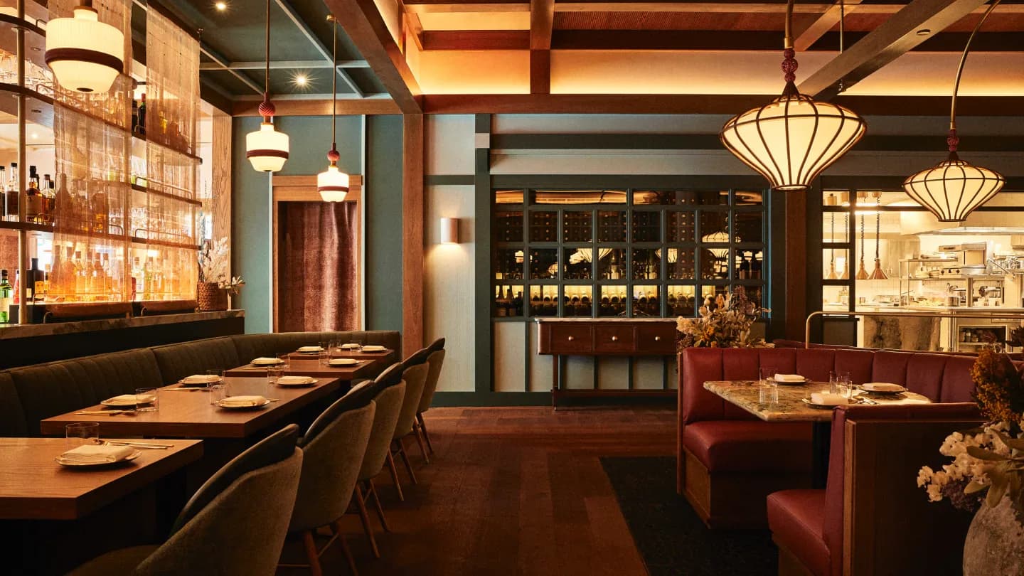 Upscale Asian restaurant interior featuring wood paneling, warm amber lighting, red banquette seating, and pendant fixtures, designed by Adam Farmerie.