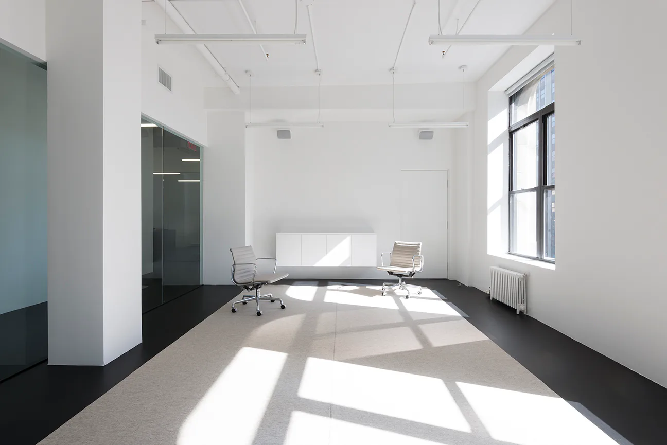 Minimalist office interior with white walls, black flooring, and natural light casting geometric shadows, designed by Adam Frampton.