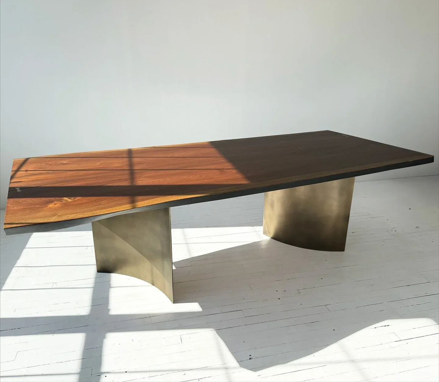 Modern concrete and wood dining table with mixed materials under natural light, designed by Adam Johnson.
