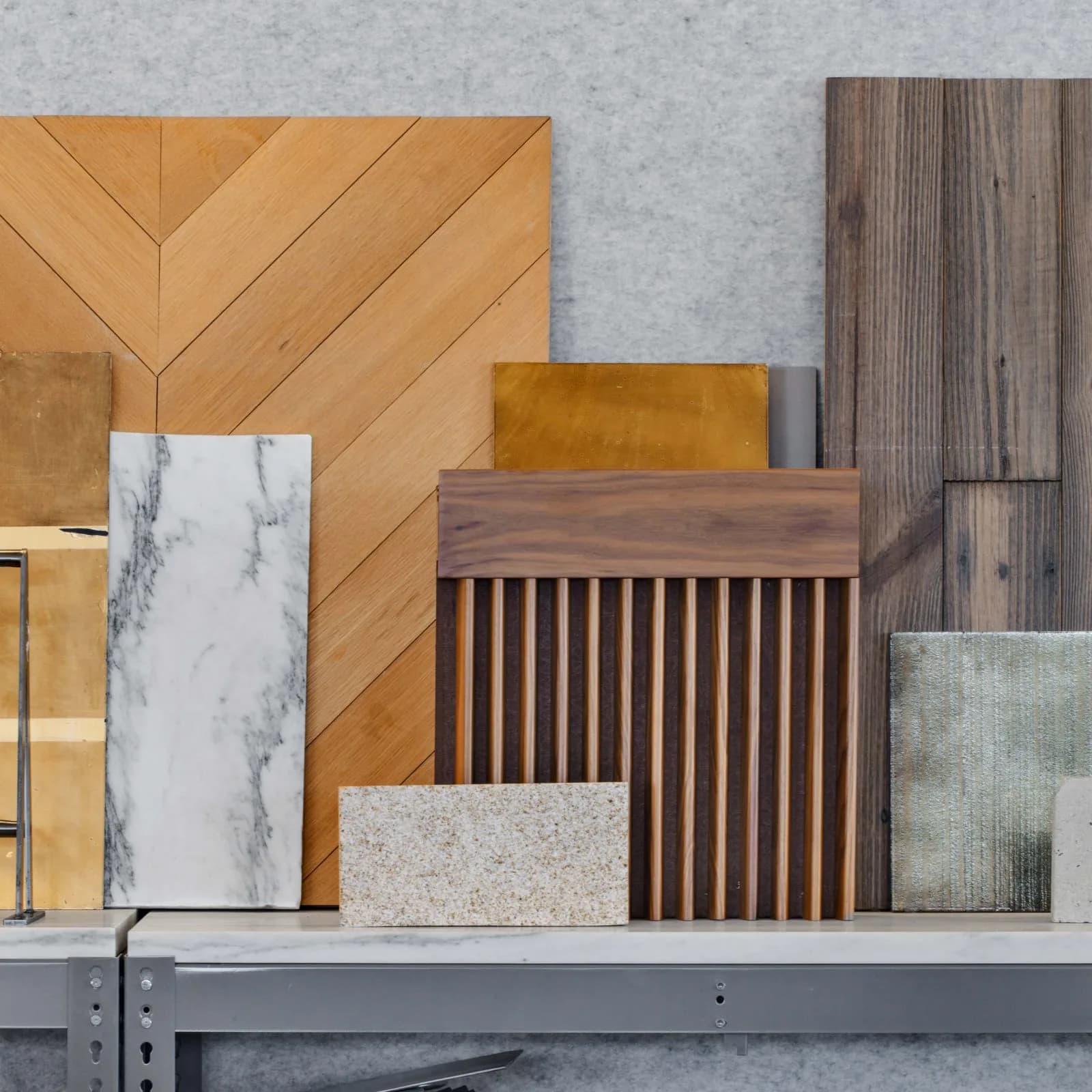 Material sample display featuring wood flooring, marble, terrazzo, and dark wood finishes arranged on a shelf by Adam Rolston.