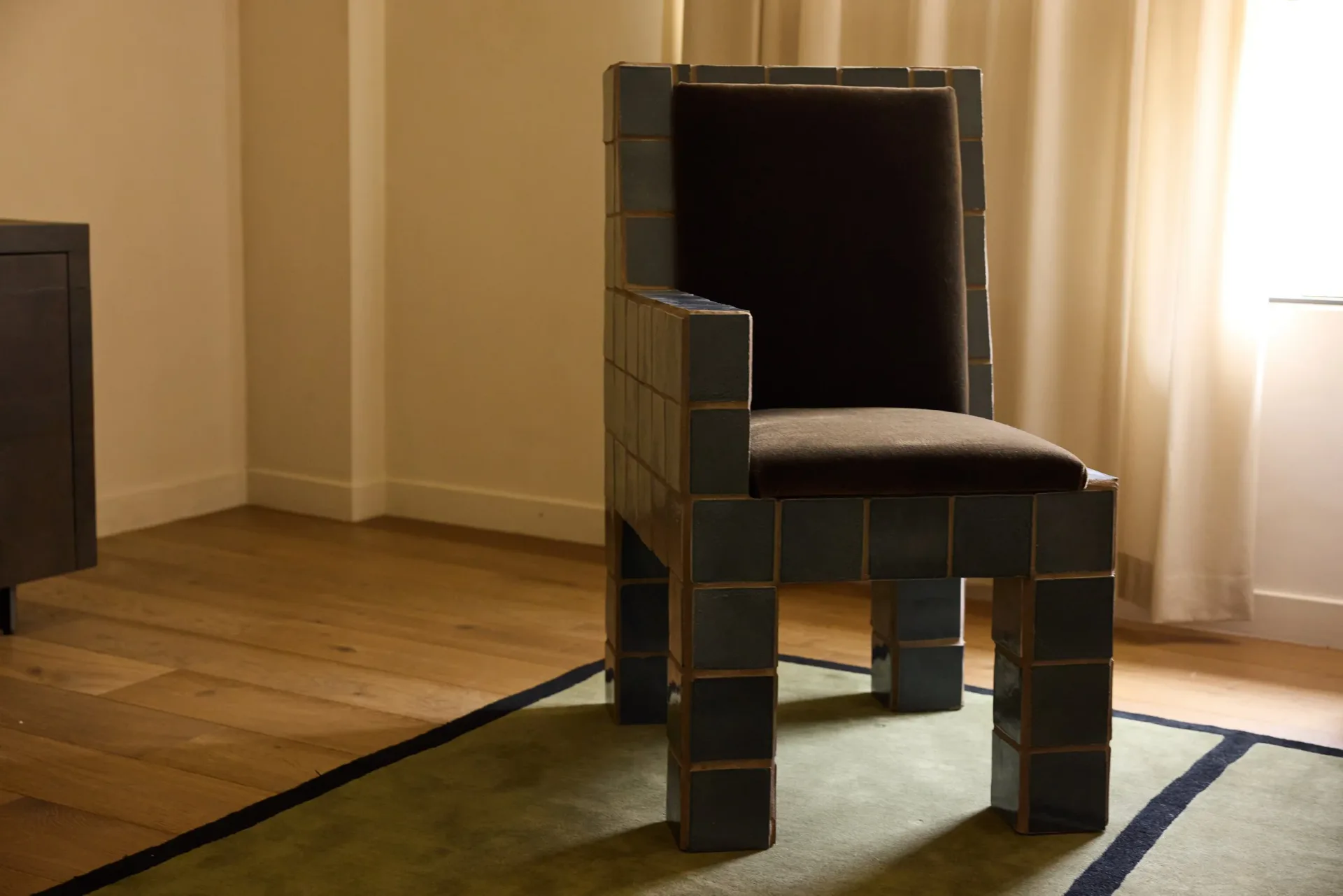 Contemporary interior featuring a sculptural dark leather chair with geometric wooden block base on a minimalist concrete floor, designed by Ah Um Design Studio.