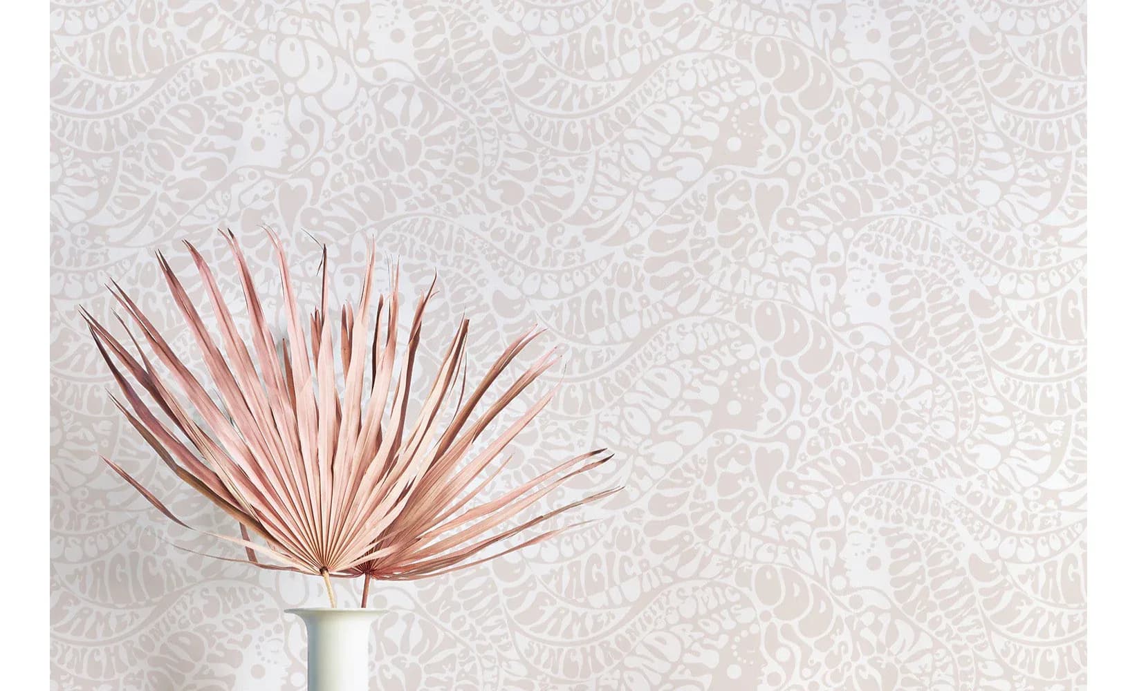 Dried pink palm frond in white vase against patterned wallpaper, styled interior design by Aimee Wilder.