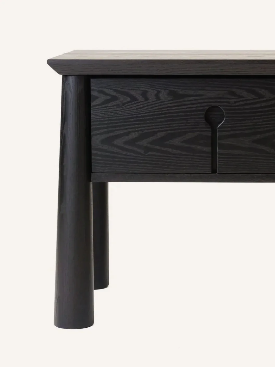 Detail of a black stained wood table with cylindrical legs and a drawer featuring a simple round pull, by Alara Alkan.