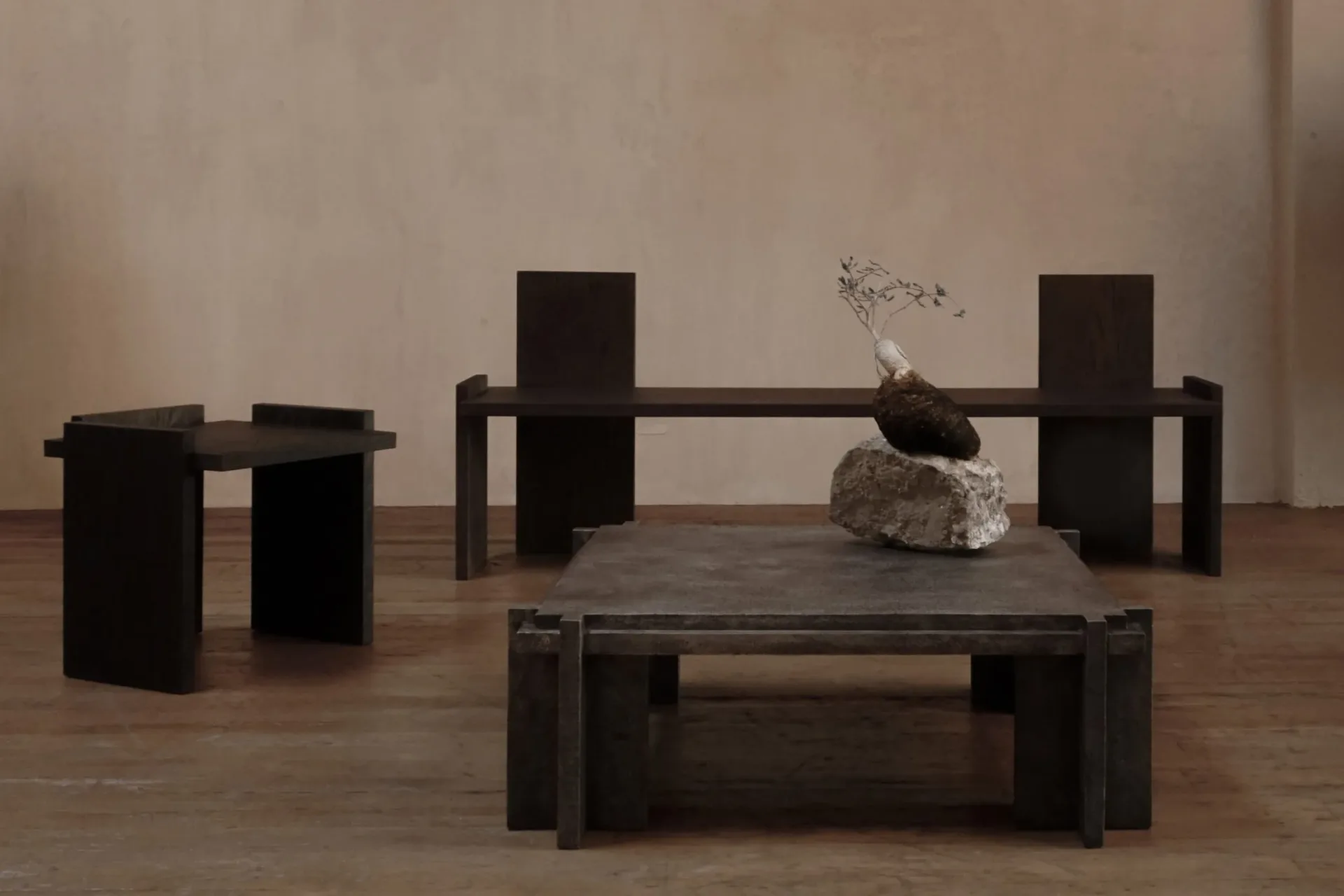 Dark minimalist furniture installation with black geometric forms including cubes, platforms, and a bench arranged in a sparse gallery space by Alejandro Bataille.