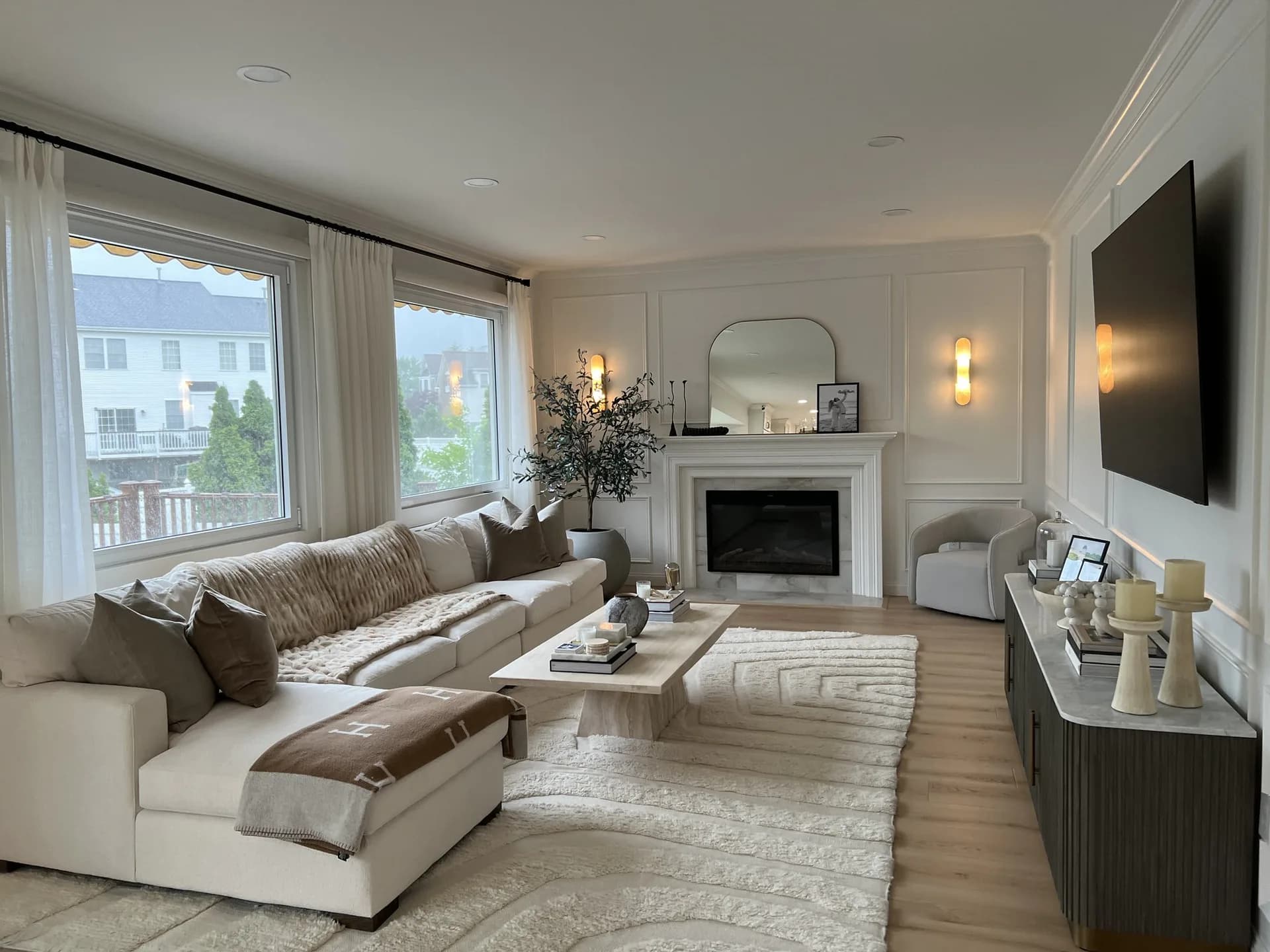 Bright modern living room with cream sectional sofa, fireplace, large windows, and neutral wood flooring by Alex Hurwitz.
