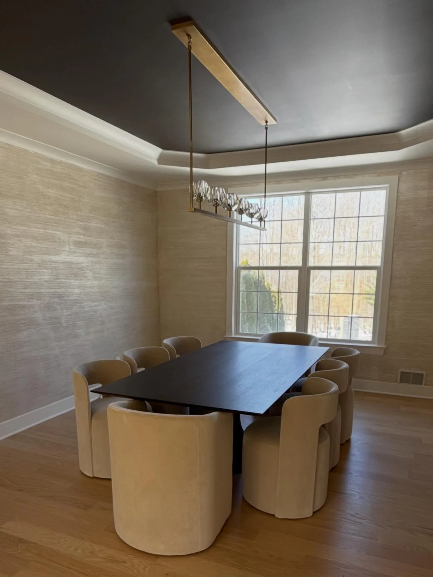 Modern dining room with curved cream walls, dark ceiling, black table with cylindrical cream chairs, and a linear pendant light, by Alex Hurwitz.