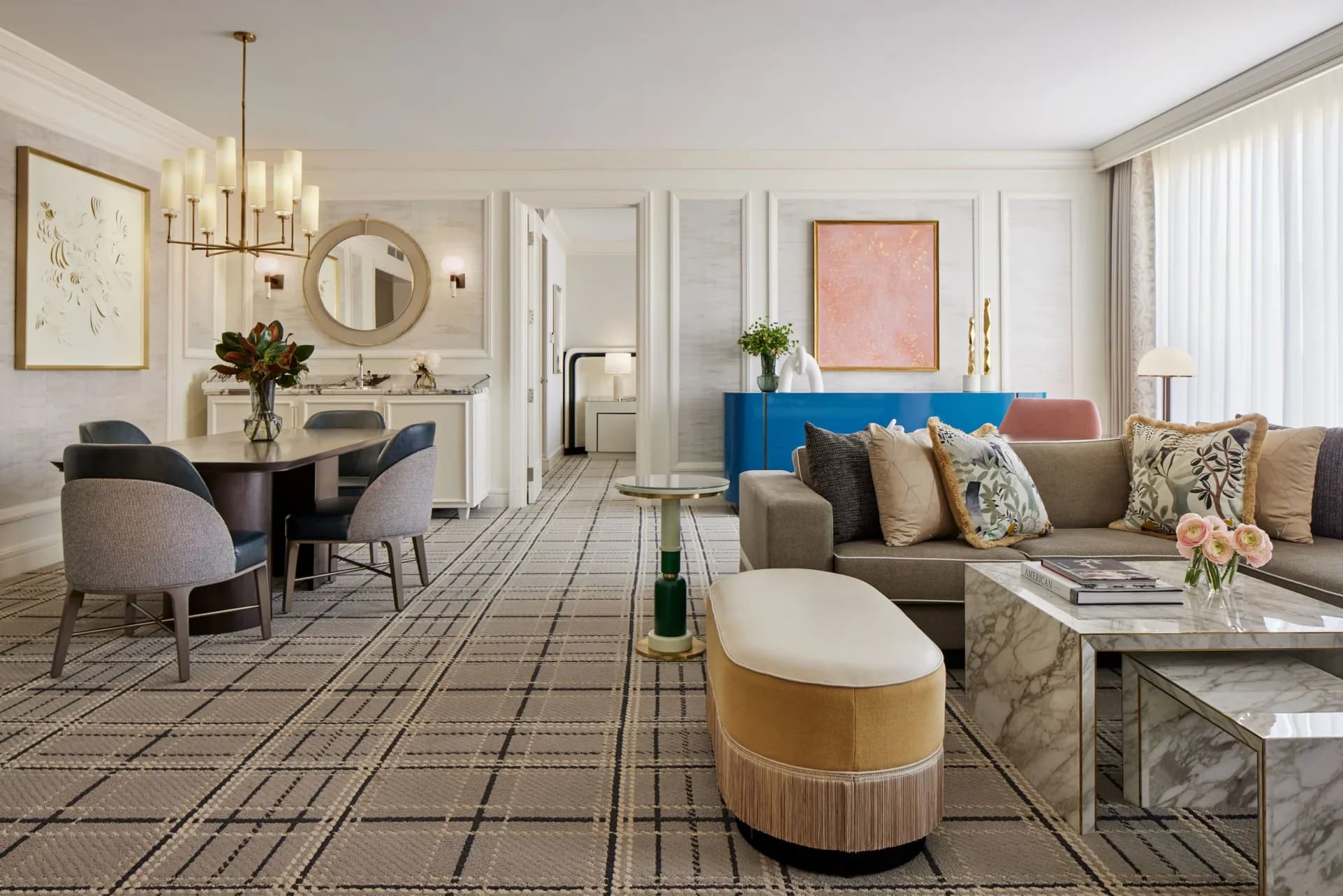 A luxurious hotel suite living room features a gray sofa, blue accent wall, marble coffee table, and elegant furnishings in neutral tones by Alexandra Champalimaud.