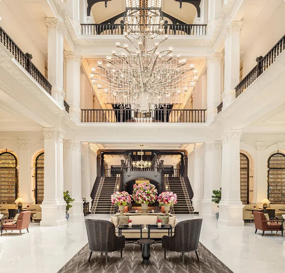Grand hotel lobby with soaring white columns, crystal chandeliers, symmetrical staircases, and floral arrangements by Alexandra Champalimaud.