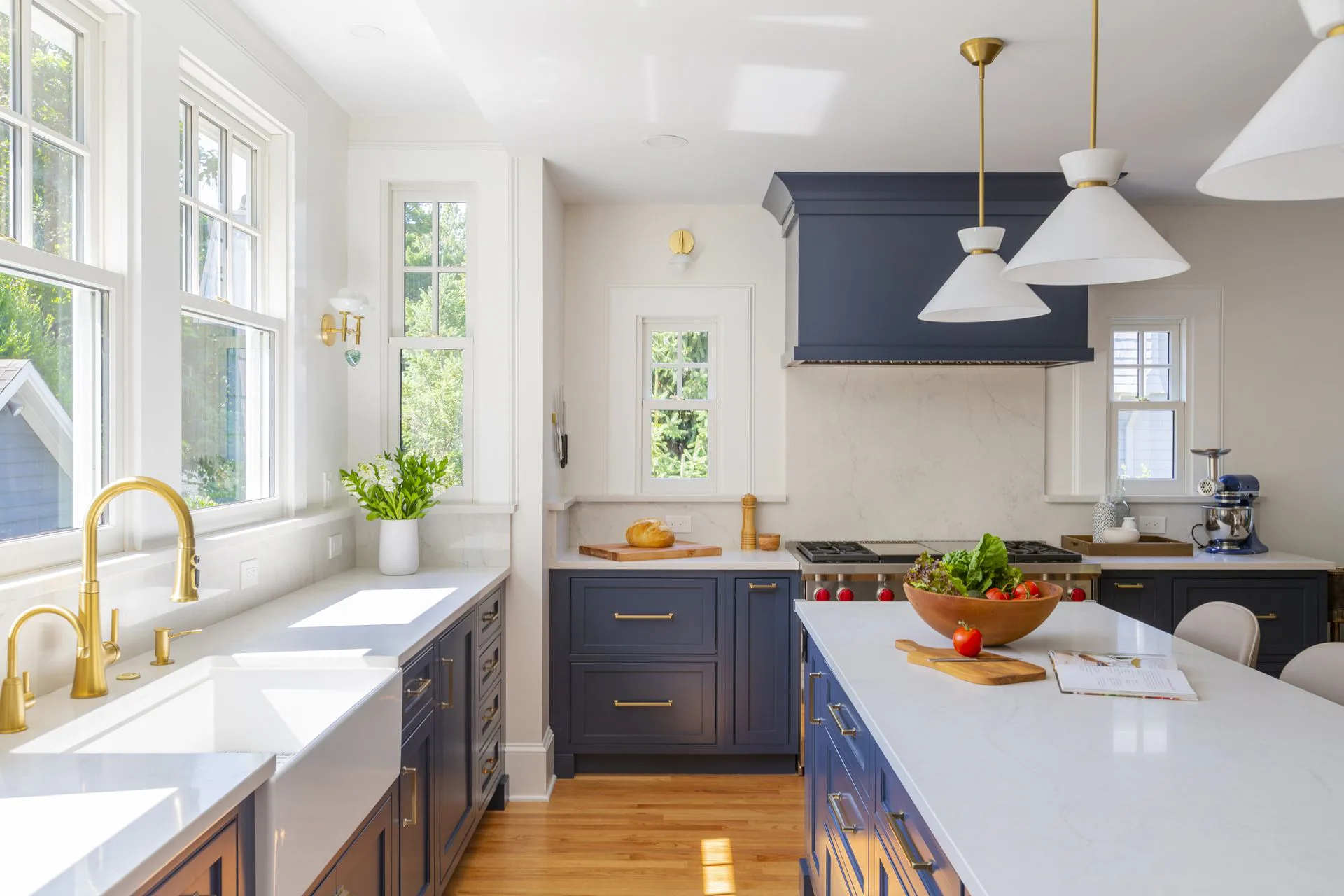 Modern kitchen with navy cabinetry, white marble countertops, brass fixtures, and pendant lighting by Alexandra Grosser.