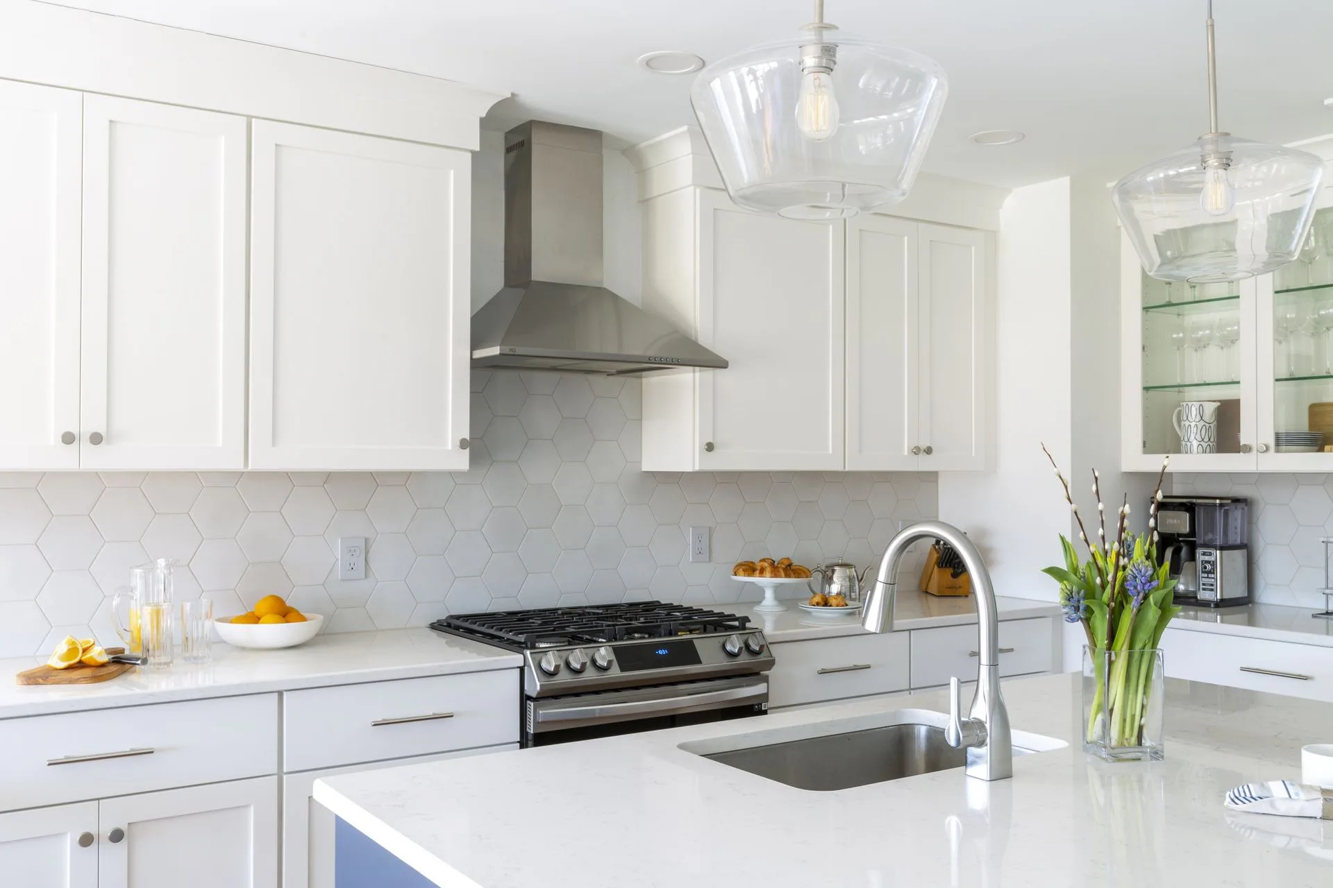 Bright white modern kitchen with marble countertops, stainless steel range hood, gas cooktop, and white cabinetry by Alexandra Grosser.
