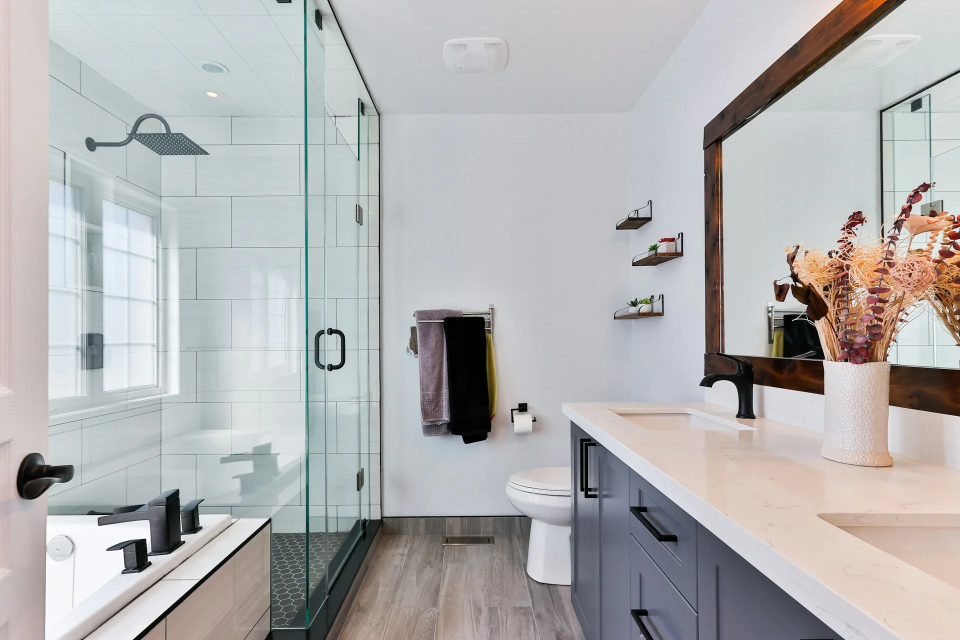 Modern bathroom with white subway tile shower, gray vanity, white quartz countertop, and wood-look flooring designed by Alexandra Grosser.