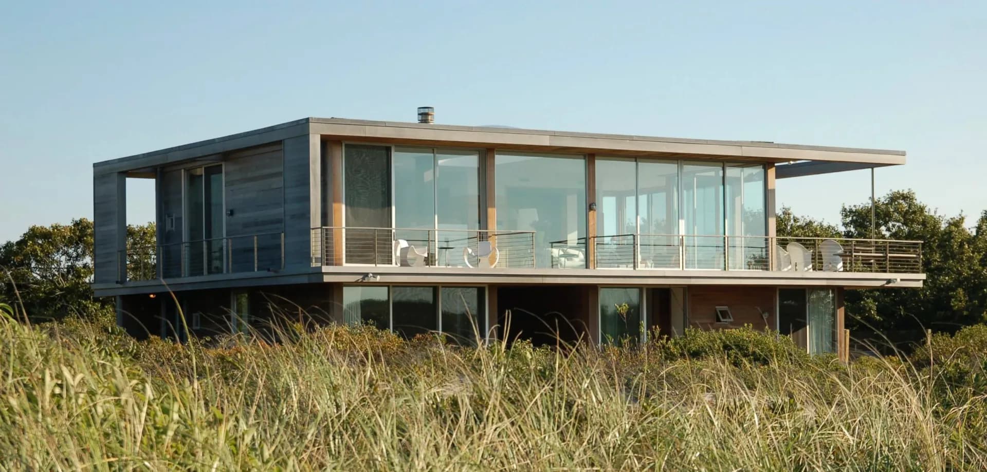 Modern elevated residential architecture with dark metal framing and extensive glazing overlooking coastal grassland by Alexi Simmons.