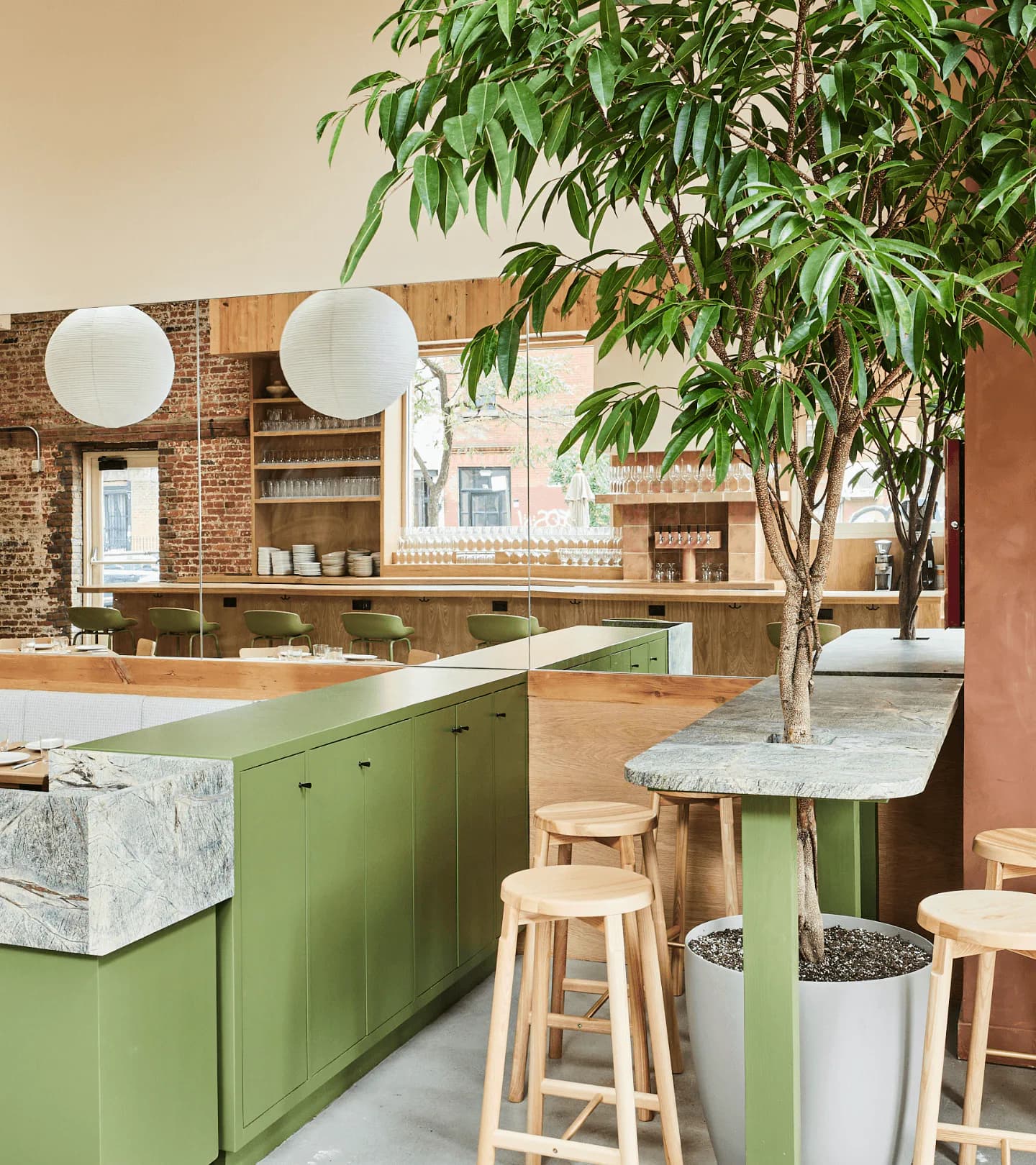Modern kitchen with sage green cabinetry, marble countertops, and a living ficus tree integrated into the dining space by Alia Marzuki.