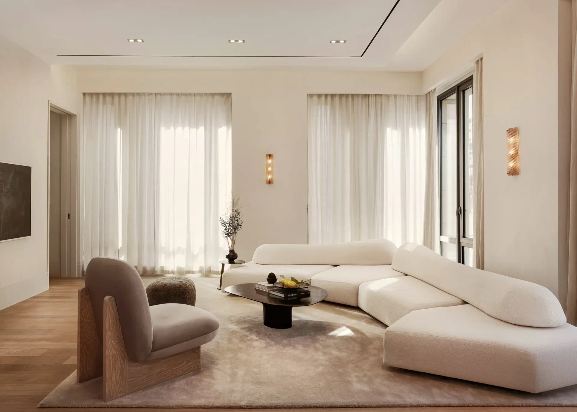 Minimalist living room with curved cream furniture, wooden flooring, large windows with sheer curtains, and soft neutral tones by Alina Pimkina.