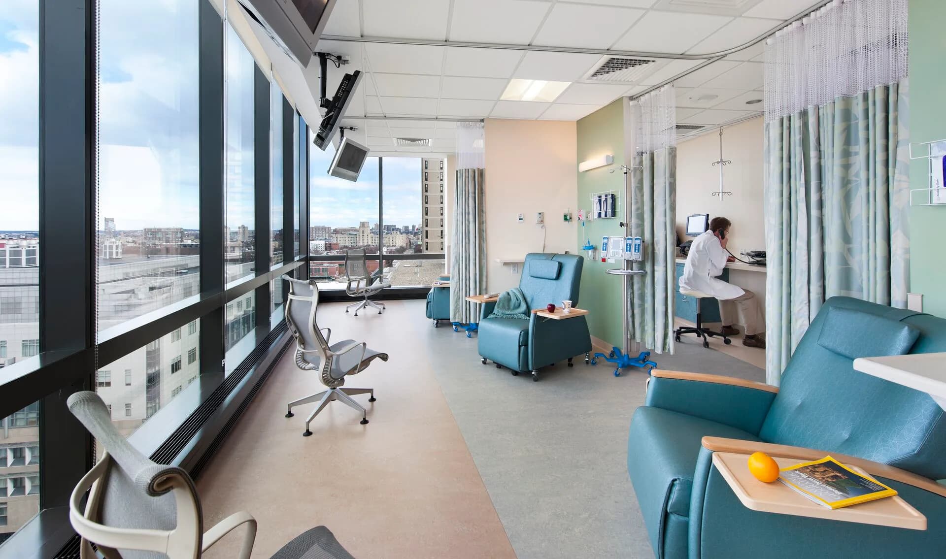 Modern medical clinic interior with floor-to-ceiling windows, turquoise seating, white ceiling, and open treatment areas by Alison Fidler.