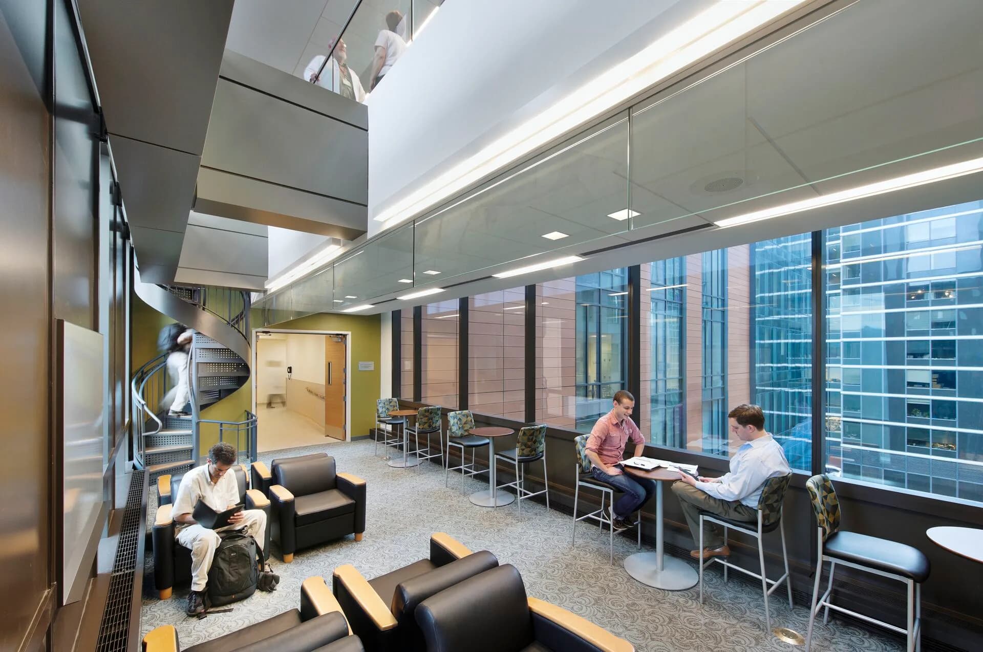 Modern office lounge with floor-to-ceiling windows, black seating, yellow accent wall, and skyline views by Alison Fidler.