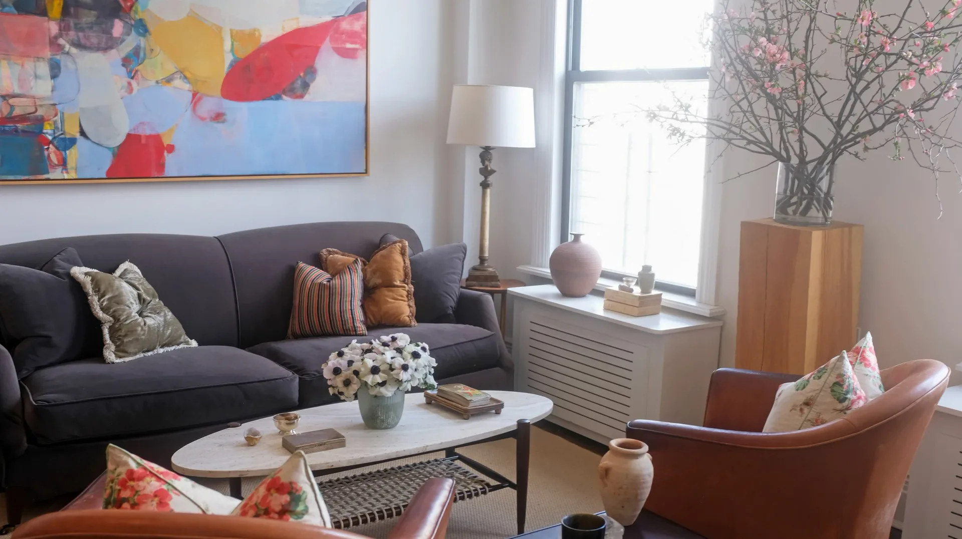 Contemporary living room with dark gray sectional, cognac leather chair, white marble coffee table, and colorful abstract artwork, designed by Allison Alexander.
