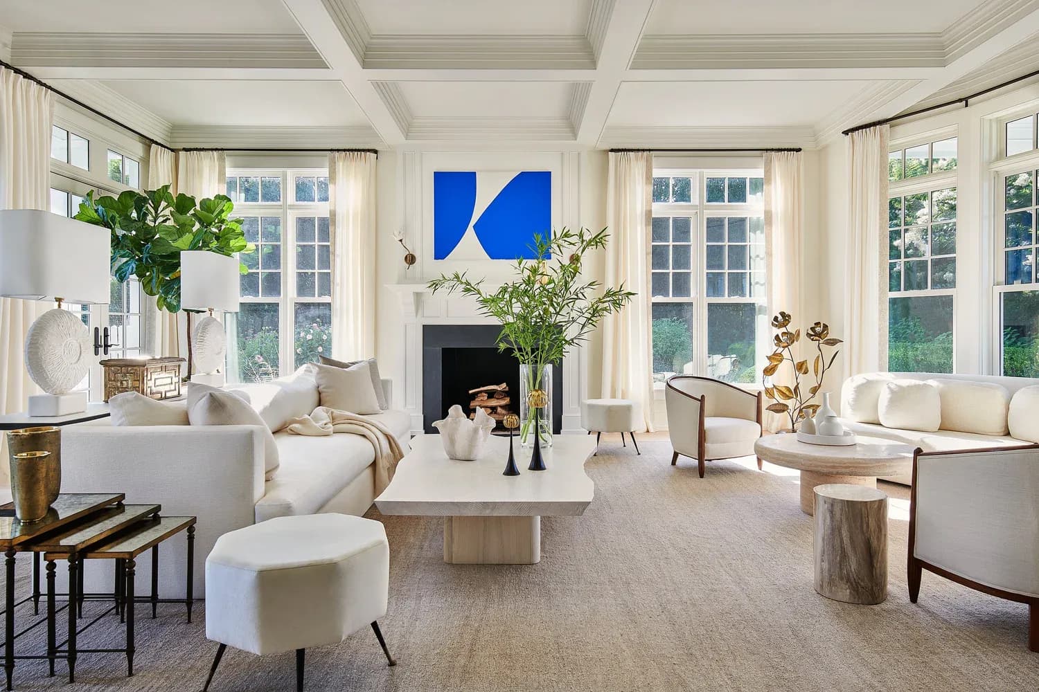 Bright, minimalist living room with coffered ceiling, cream furnishings, large windows, fireplace, and blue abstract wall art by Allison Babcock.