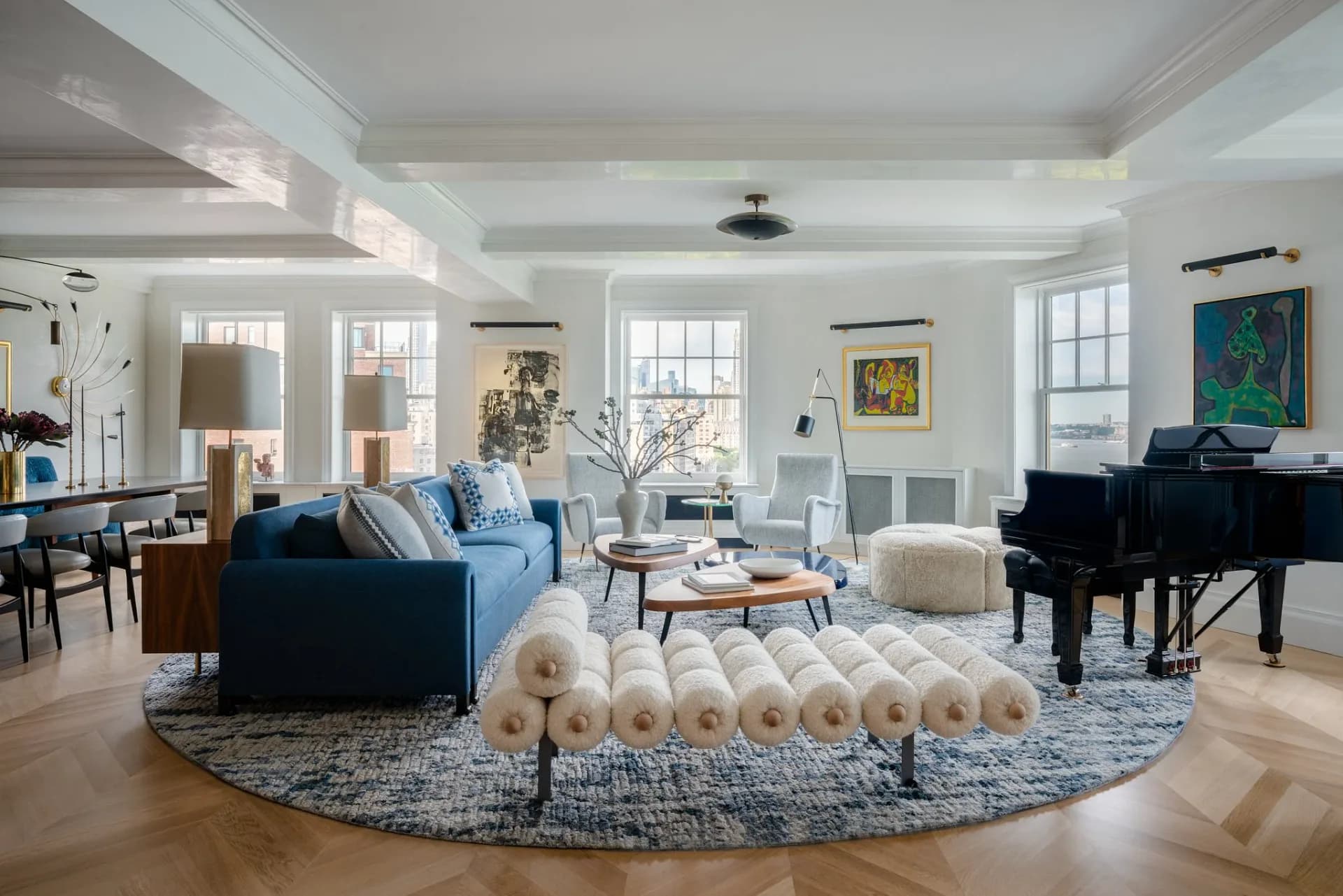Bright, airy living room with blue sofa, grand piano, round blue rug, and coffered ceiling featuring warm wood tones and natural light by Allison Babcock.
