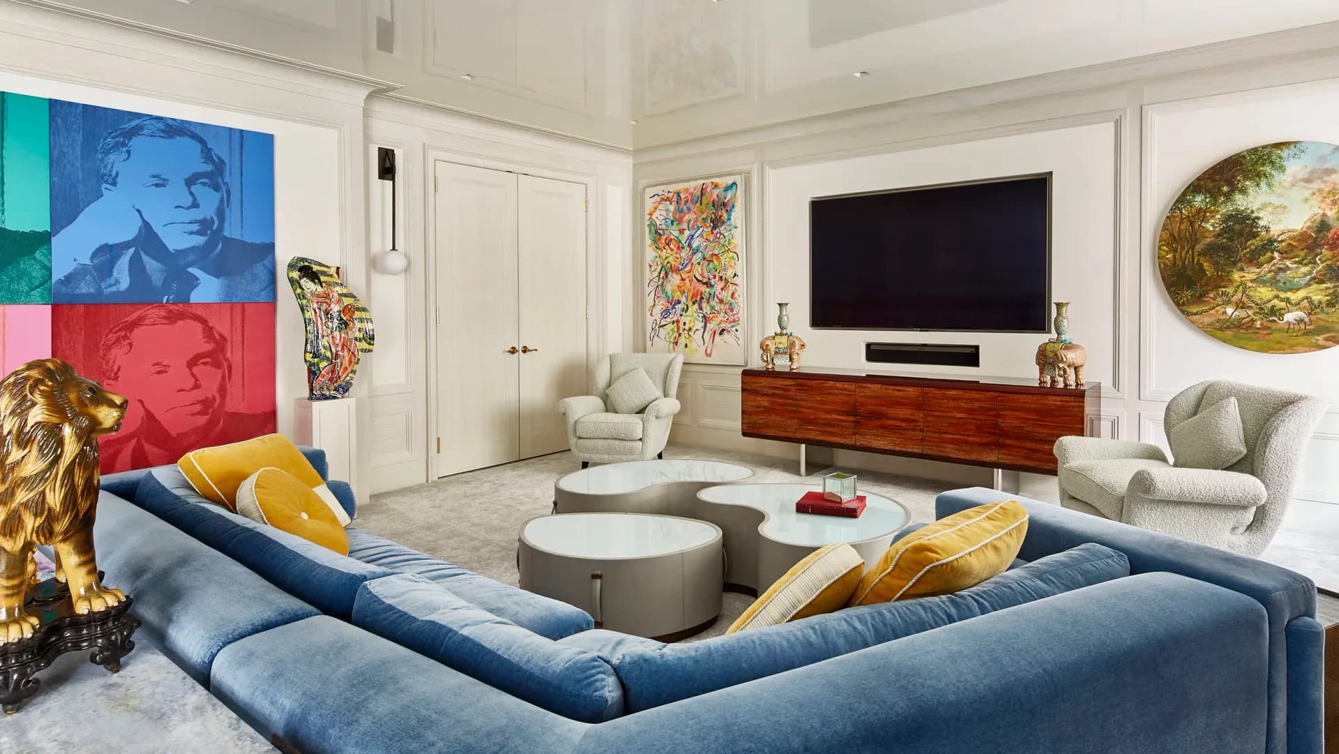 Modern living room with blue curved sofa, wood media console, pop art wall installation, and gold accents by Amanda Riha.