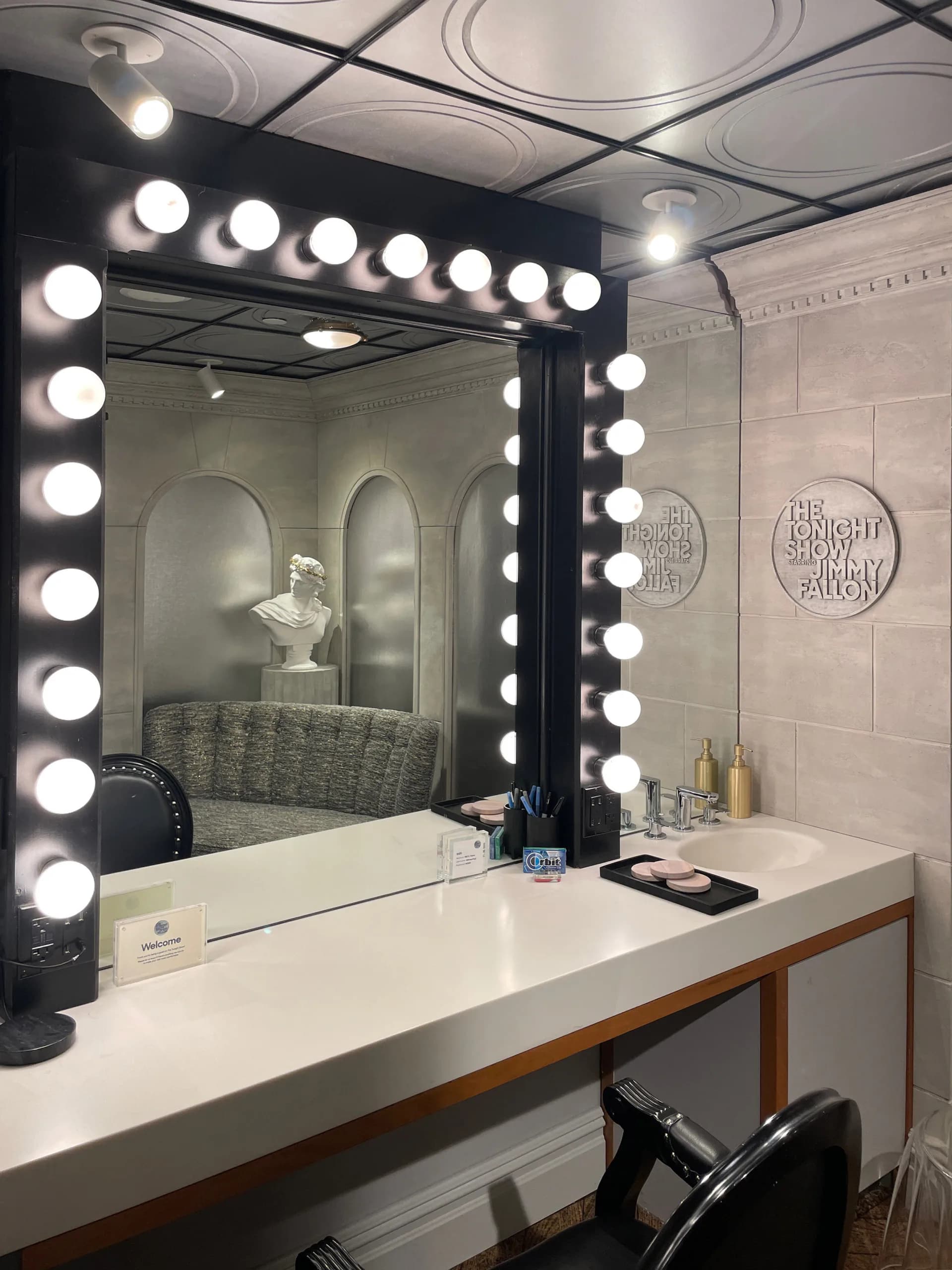 Hollywood-style vanity mirror with black frame and 20 illuminated bulbs above white countertop in modern bathroom by Amy Gavin.