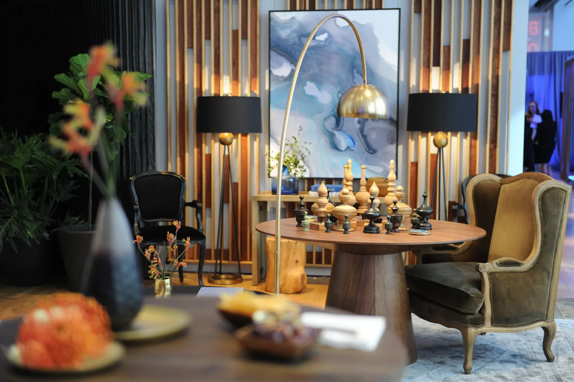 Luxe living room with golden-toned wingback chair, round wood table, and gallery wall of vertical wood slats and artwork, designed by Amy Gavin.