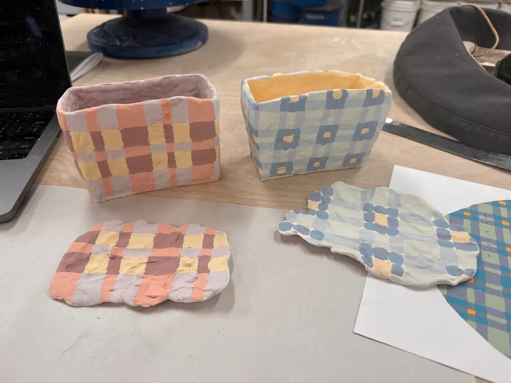 Fabric textile samples featuring geometric plaid and argyle patterns in warm and cool color palettes, displayed on a workspace by Amy Helfand.