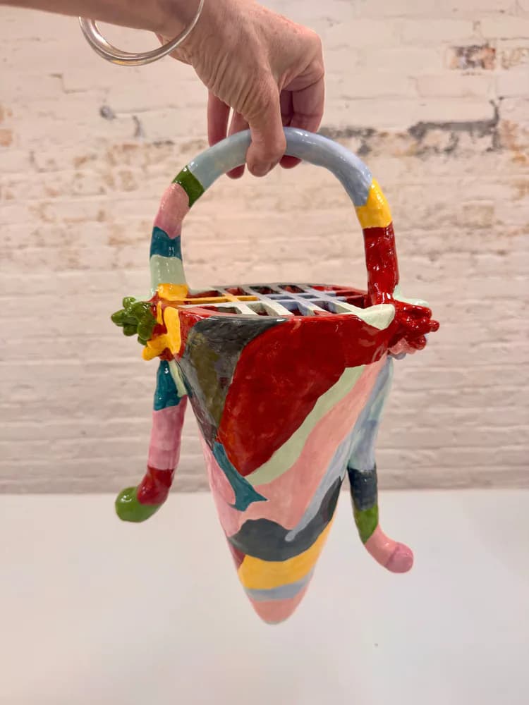 Colorful fabric textile art piece with striped handle and red velvet detail held up against white brick wall, by Amy Helfand.