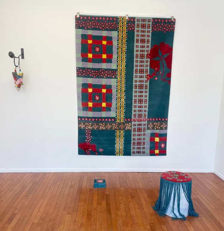 Gallery installation featuring a large textile wall hanging with geometric patterns in red, blue, and yellow, alongside sculptural floor pieces, by Amy Helfand.