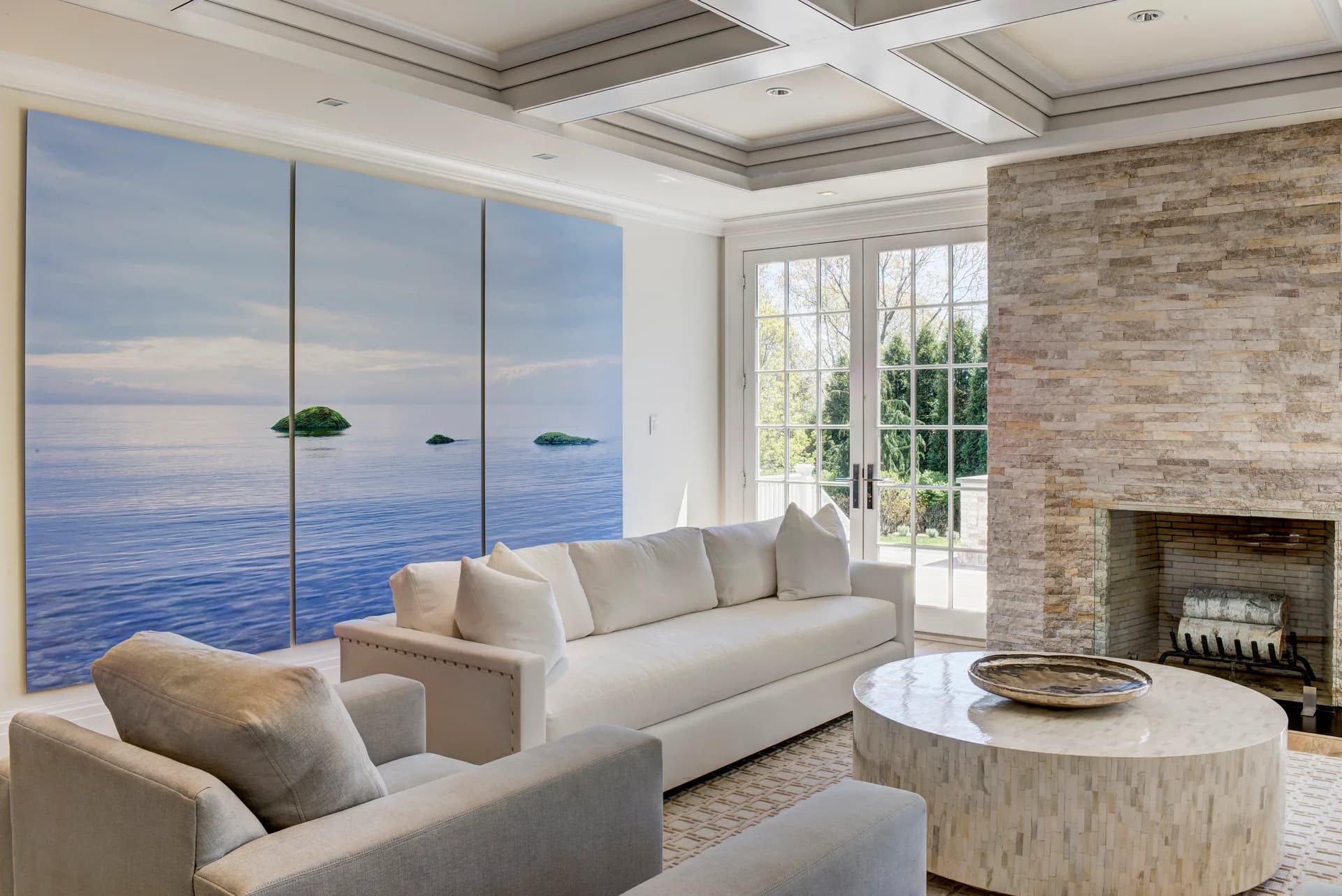 Coastal living room with cream sectional sofa, marble round table, fireplace, and expansive ocean-view windows by Amy Hill.
