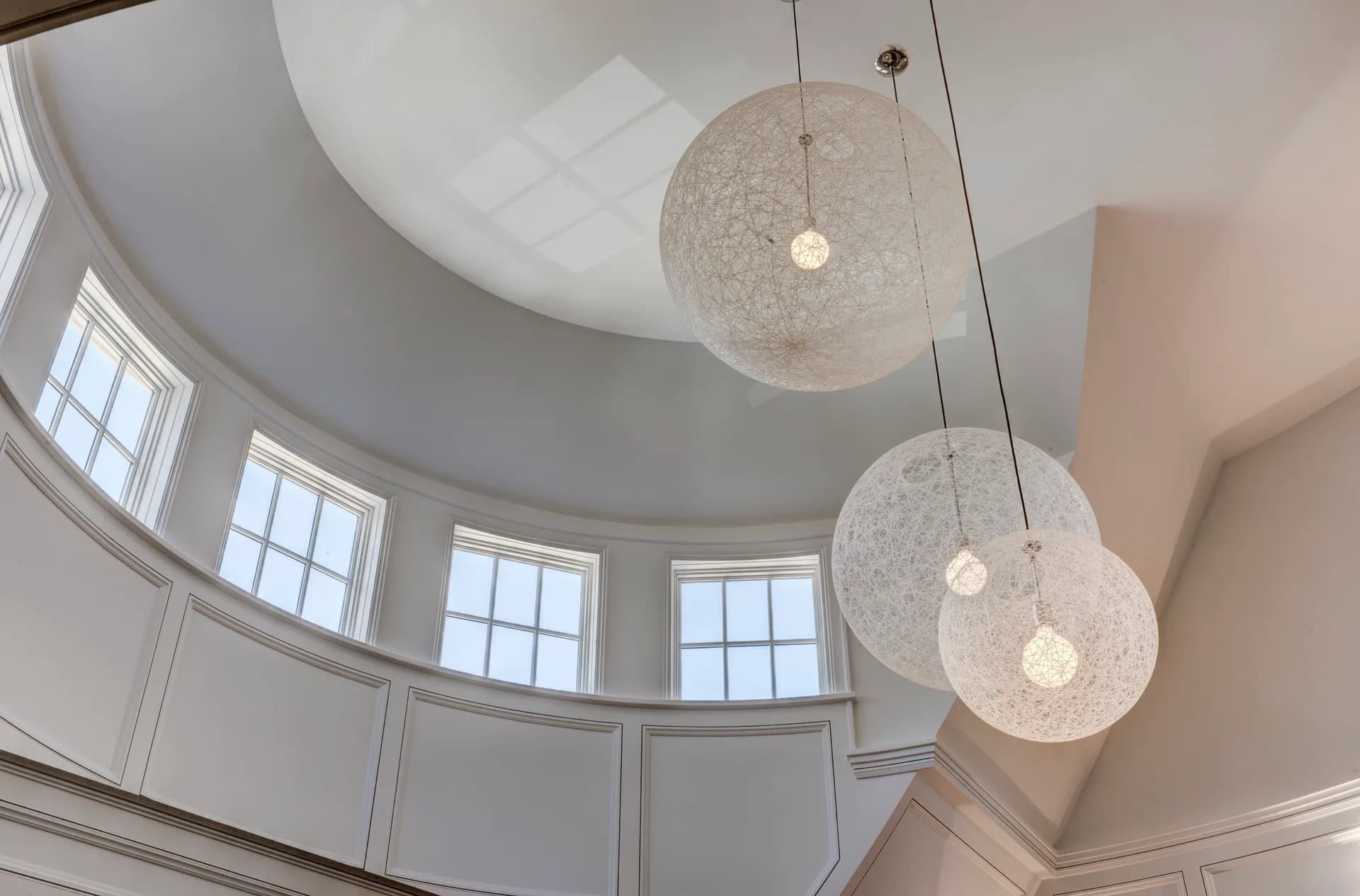 Modern entryway with curved ceiling, pendant globe lighting fixtures, and arched windows, designed by Amy Hill.