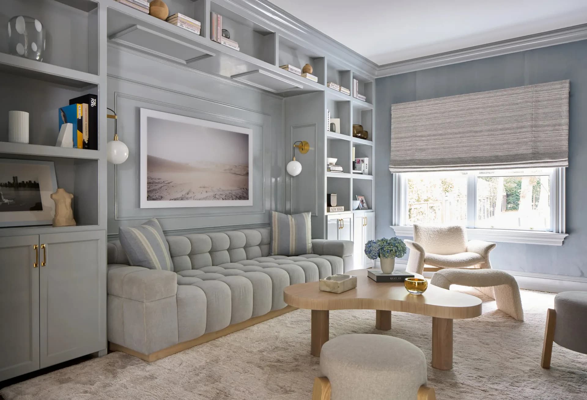 Modern living room with quilted gray sofa, built-in shelving, wooden coffee table, and cream armchair by Ana Junco.