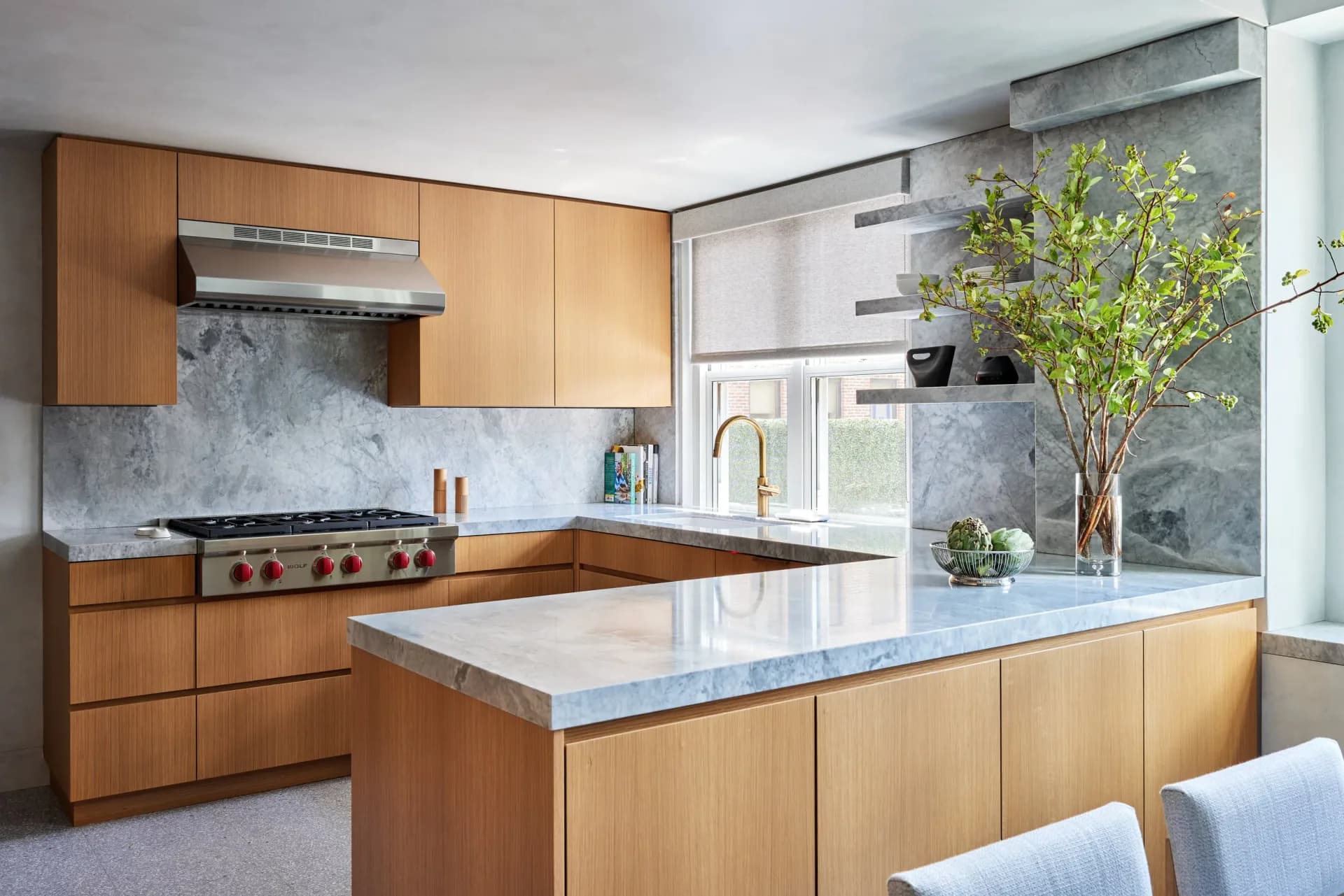 Contemporary kitchen with light wood cabinetry, marble waterfall island countertop, and blue-gray marble backsplash by Ana Junco.