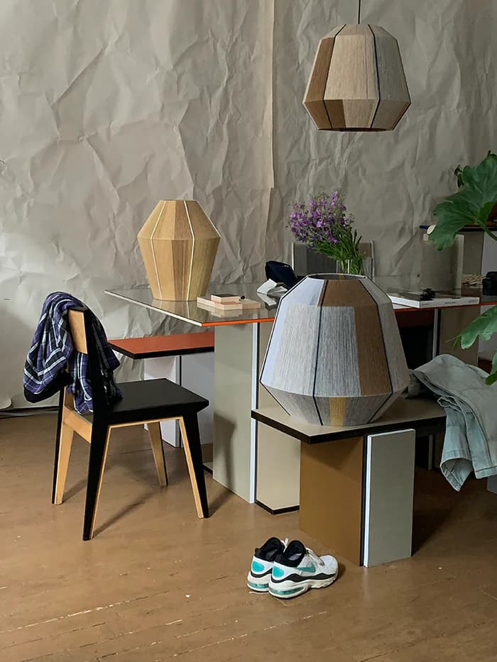 Modern interior installation featuring geometric wooden pendant lamps and sculptural lighting fixtures suspended above minimalist furniture with plants and accessories by Ana Kraš.