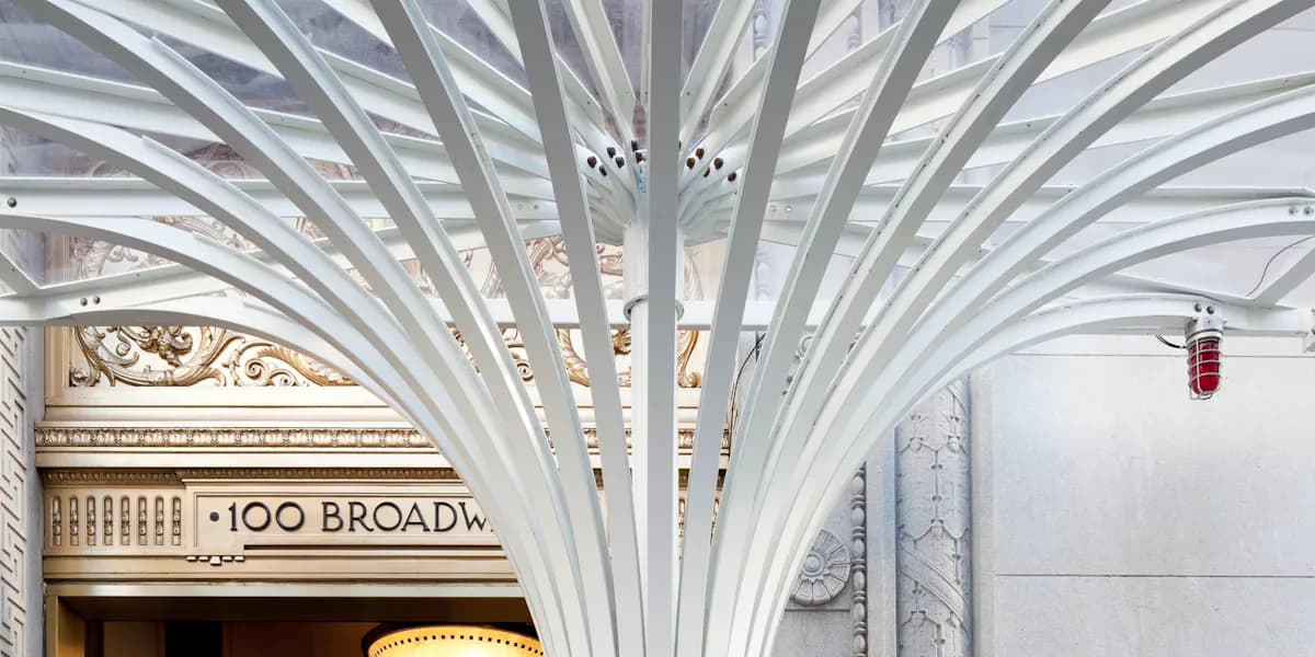 Dramatic white ribbed ceiling structure with geometric radiating pattern above a corridor entrance marked '100 BROADWAY' by Ana Rojas.