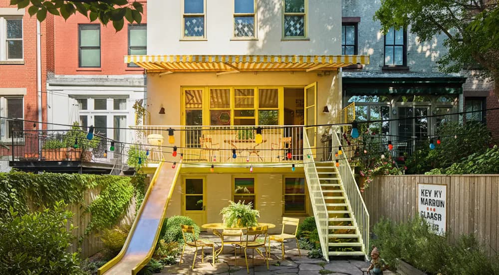 Bright yellow residential renovation with multi-level deck, outdoor seating, and integrated landscaping in an urban setting by Ana Rojas.