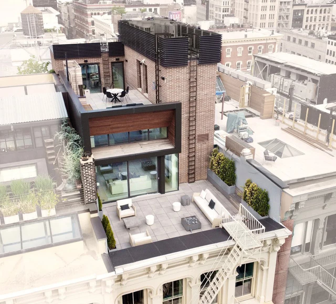 Modern rooftop residential addition with brick and glass facades overlooking city streets, featuring terraced outdoor space by Anam Ahmed.