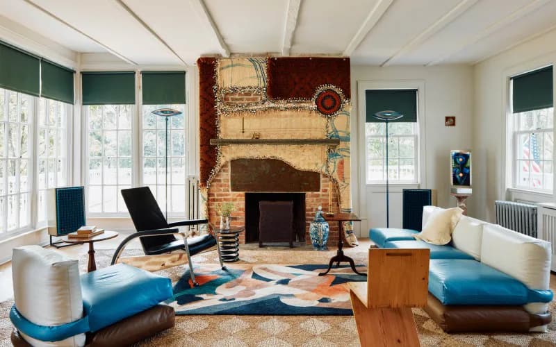 Bright modern living room with brick fireplace, blue seating platforms, geometric area rug, and large windows by Andre Herrero.