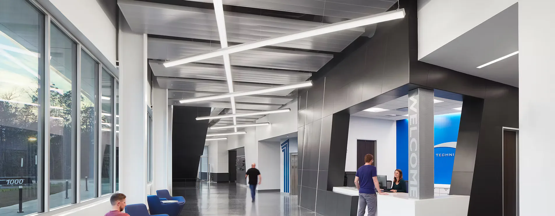 Modern institutional corridor with linear ceiling fixtures, dark accent walls, blue accent panels, and people figures positioned throughout the bright, minimalist space by Andrea Hartranft.