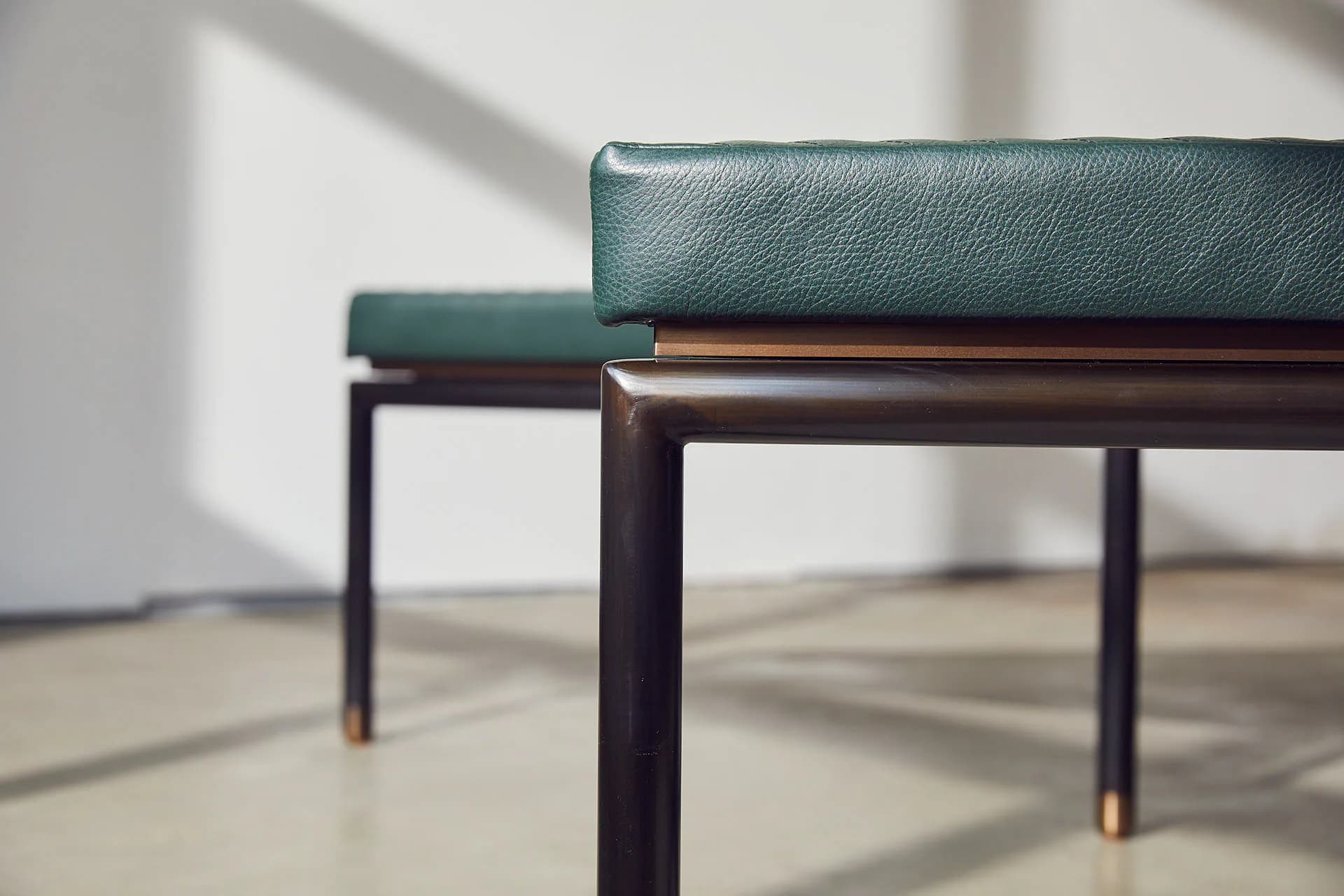 Modern furniture detail showing teal leather seating with dark metal frame and brass accents on light flooring by Andrew Baccon.