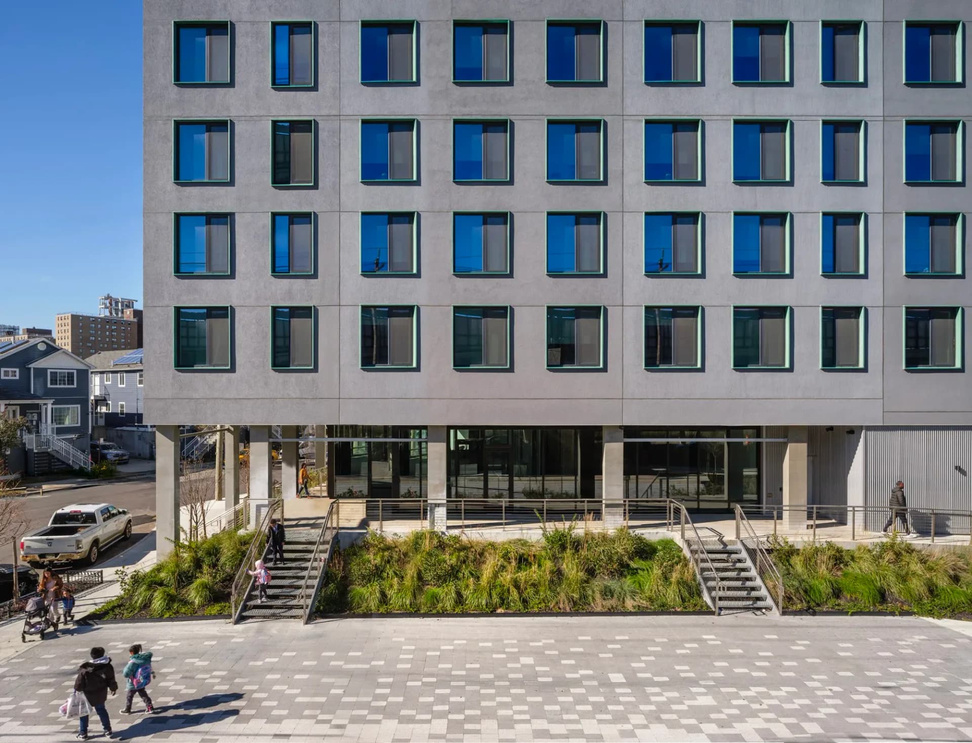 Contemporary residential building with gridded facade, ground-level public plaza with landscaping and seating areas by Andrew Bernheimer.