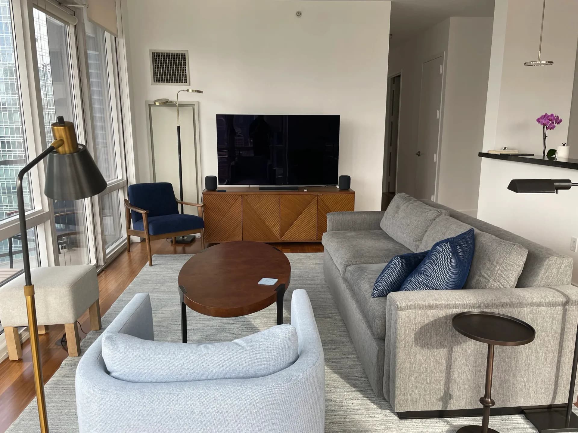 Modern living room with curved cream sectional, wooden TV console, round coffee table, and blue accent chair by Andy Schwalen.