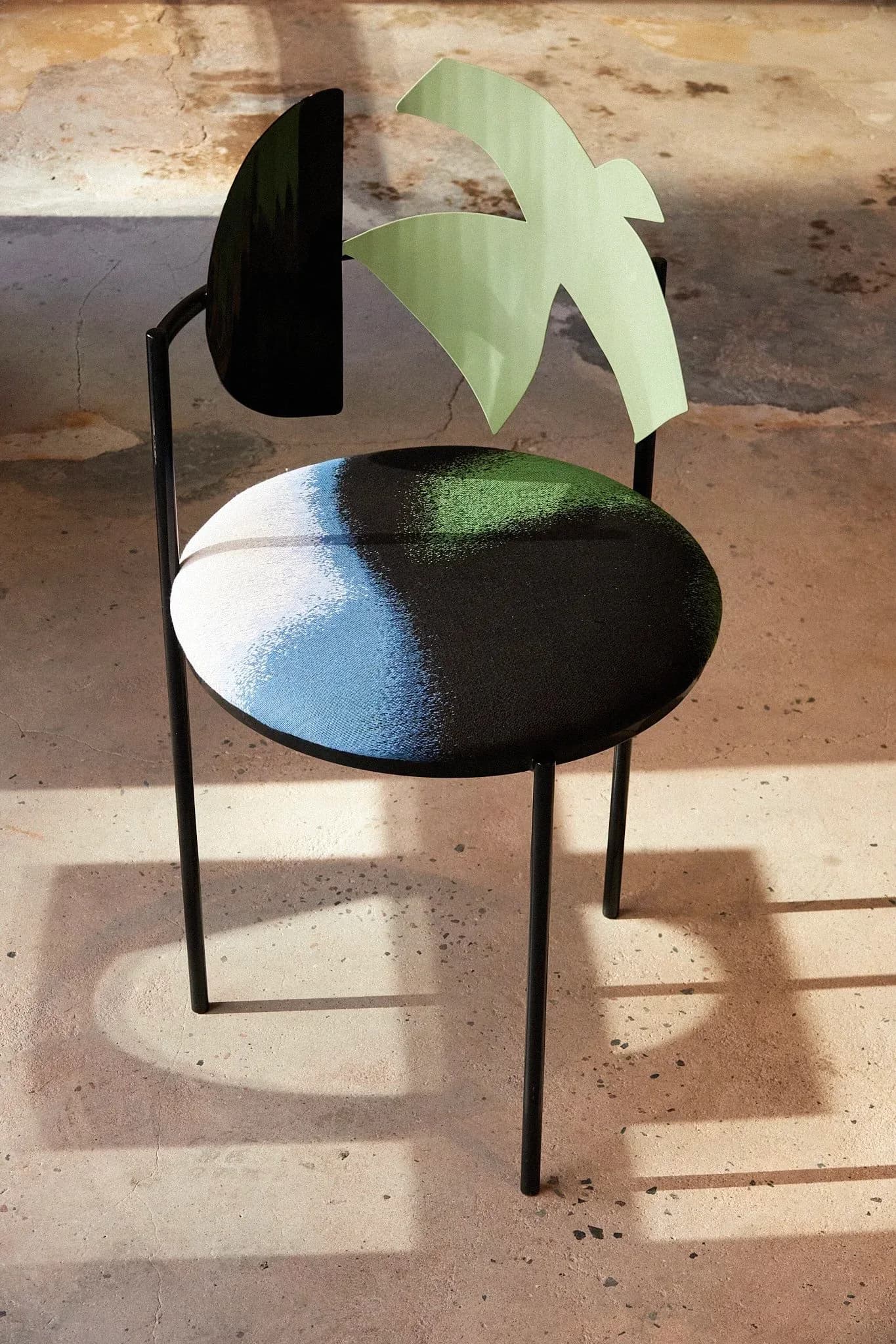 Sculptural chair with black metal frame, colorful painted seat in blue, white, and black, and organic green leaf-shaped backrest by Angel Mombiedro (Armombiedro Studio).