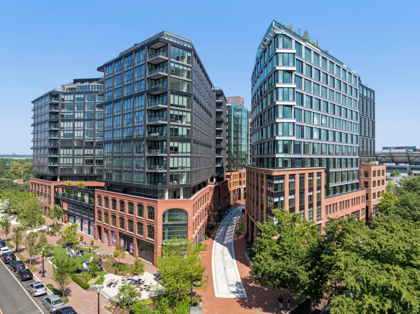 Mixed-use urban development with red brick historic buildings and modern glass tower residential structures surrounding a central courtyard plaza by Angela Liu.