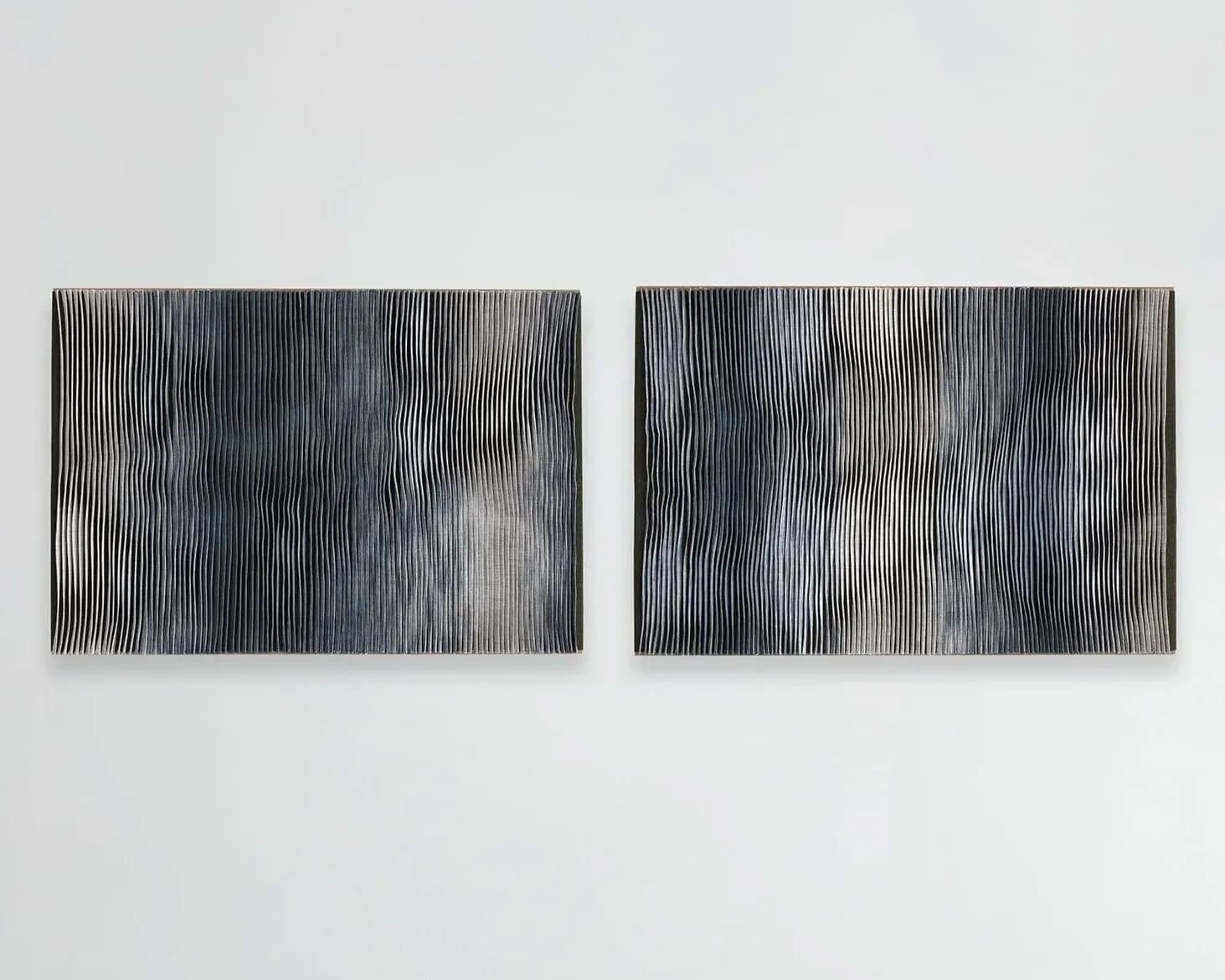 Two abstract linear wall installations with vertical striations in grayscale tones, creating gestural compositions by Anjuli Bernstein.