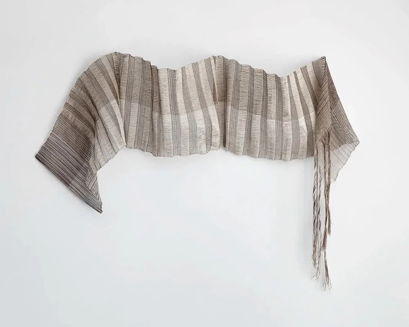 Pleated textile installation with layered striped fabric panels in neutral tones creating dimensional sculptural form by Anjuli Bernstein.