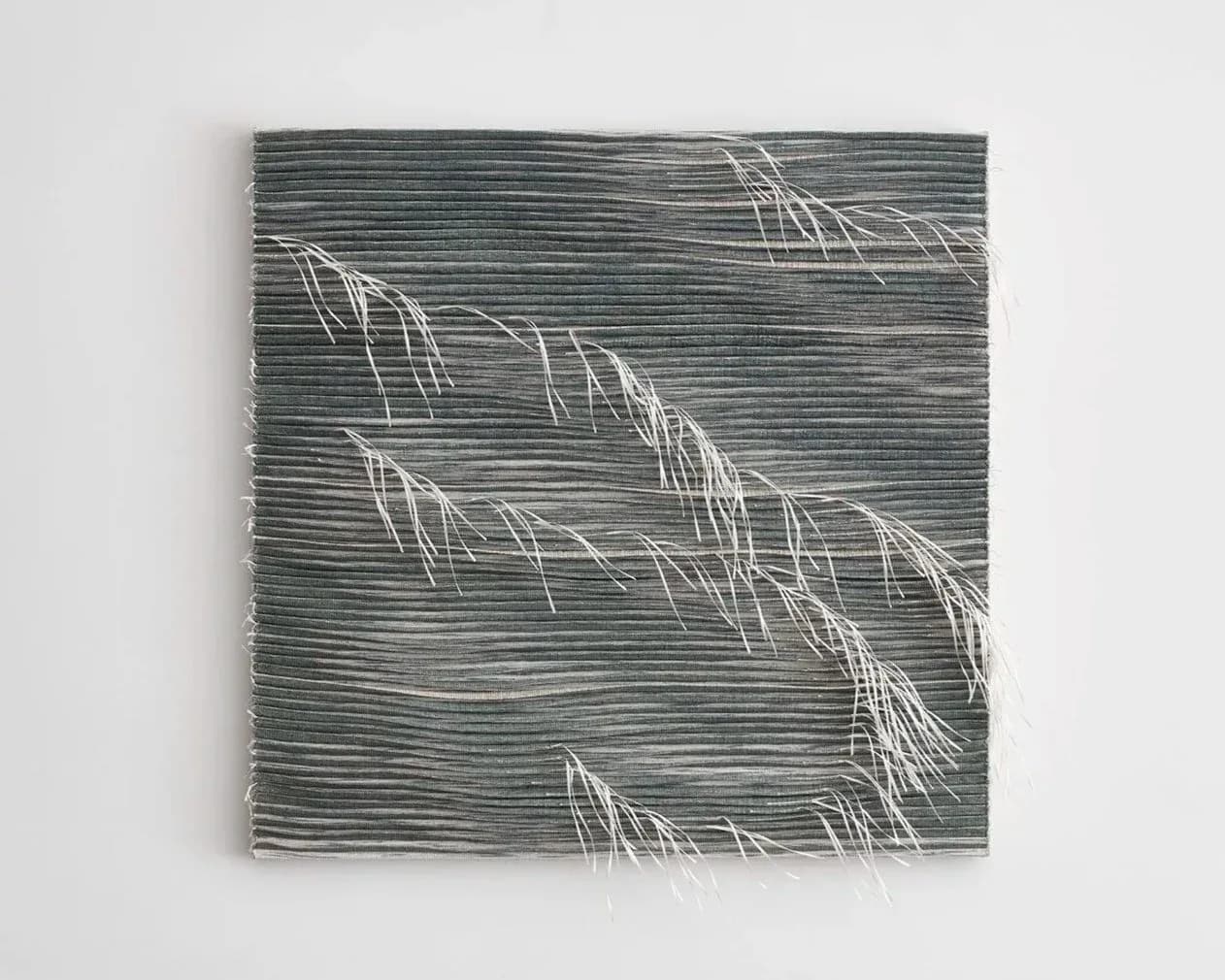 Textured wall installation with layered gray-green horizontal lines and white woven fiber elements creating dimensional botanical forms by Anjuli Bernstein.