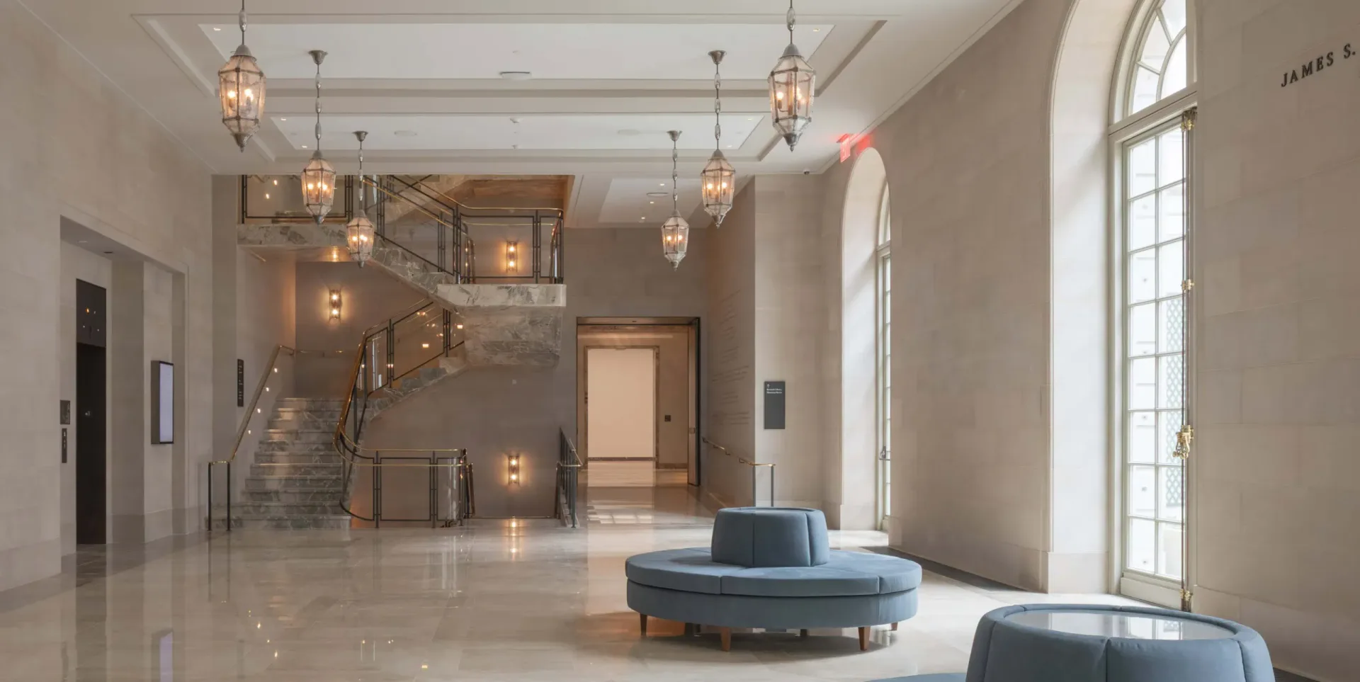 A luminous lobby with polished stone flooring, glass partitions, suspended pendant lighting, and curved seating elements in a contemporary minimalist design by Annabelle Selldorf.